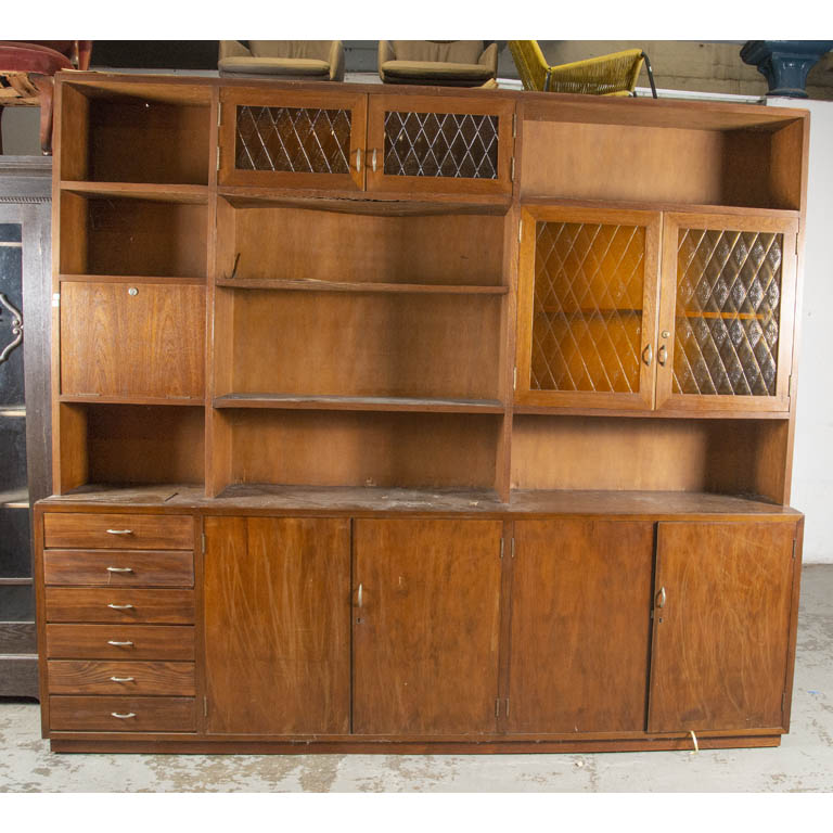Modular de nueve puertas y seis cajones. Una puerta abatible horizontal y cuatro puertas con frentes vidriados (vidrio fantasia amarillo). Varios sectores con enchapado desprendido y con averías. Detalles en el lustre. - Medidas: 261x47x230cm