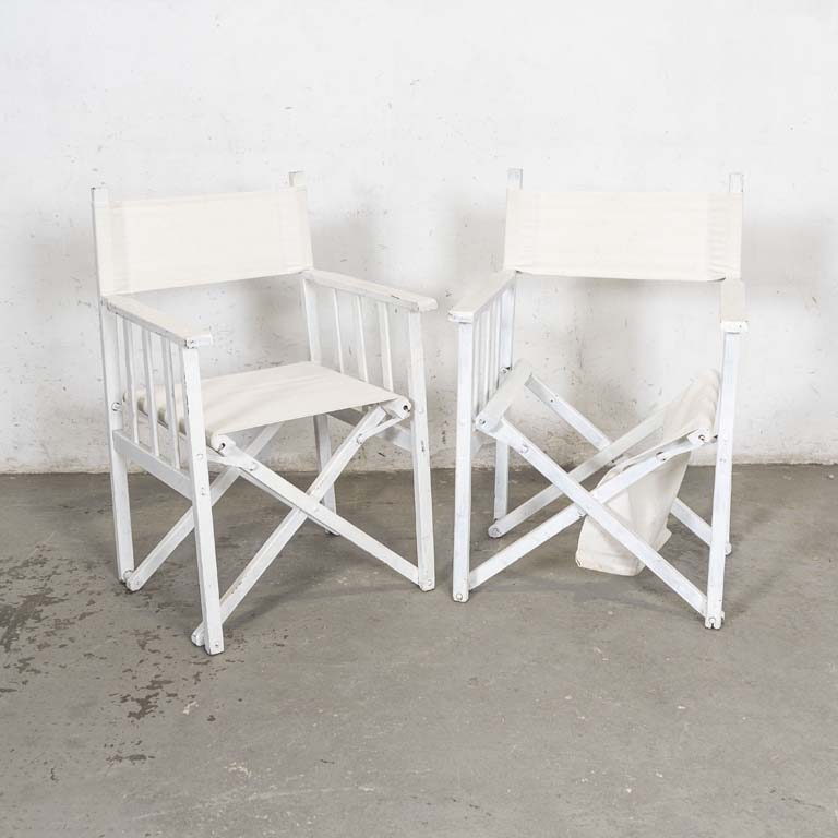 Par de sillas tipo "director", plegables . Pintadas de blanco con asientos y respaldos de lona blanca. Falta varilla del asiento para sujetar la tela, detalles en la pintura y tapizados manchados. - Medidas: 58x49x90cm