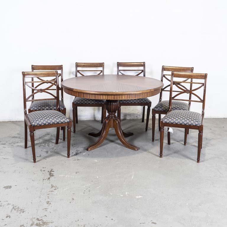 Mesa de comedor circular y seis sillas inglesas. Mesa con pie central y seis sillas con asientos tapizados. Una silla con pata desencolada. Sillas con detalles en el lustre, tapizados manchados y con desgaste. Detalles en el lustre. - Medidas: 122 x 76cm