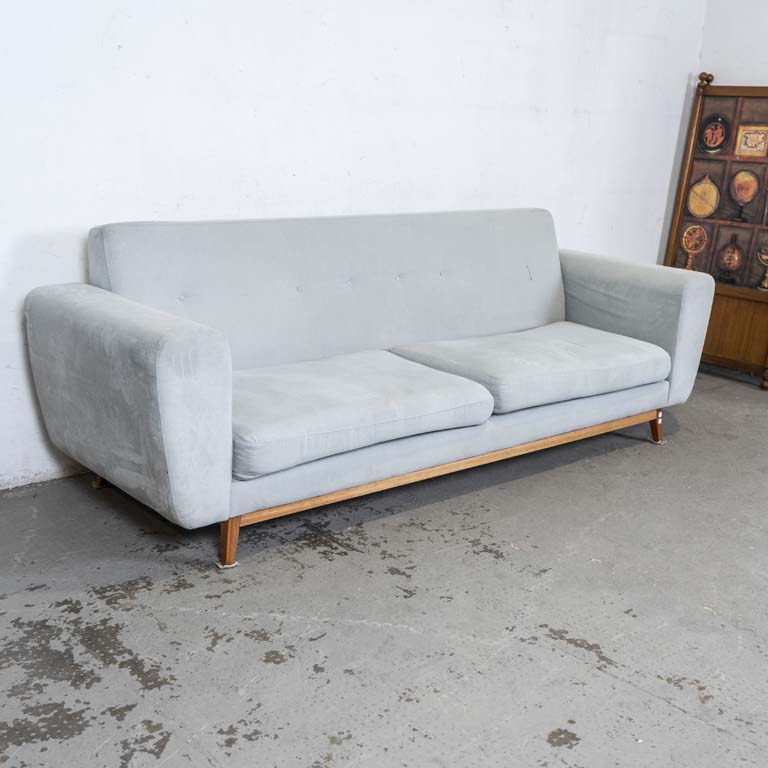 Sofá de dos cuerpos tapizado en tela celeste, con almohadones en el asiento y patas de madera. Falta botones del capitoneado, tapizado manchado (para limpiar). - Medidas: 257 x 80 x 87cm