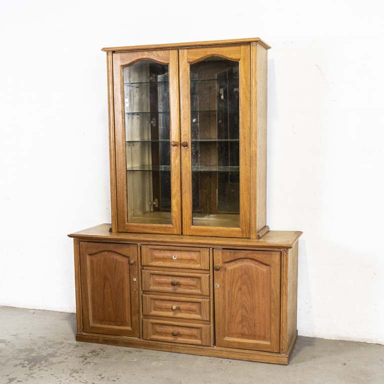Aparador cristalero en cerejeira, en dos partes. Sector superior con: dos puertas vidriadas, tres estantes de vidrio y fondo espejado. Sector inferior: cuatro cajones y dos puertas. Cajón superior trancado y sin tirador. Bisagra con avería. Detalles y marcas en la madera. Detalles en el lustre. - Medidas: 150 x 50 x 200cm