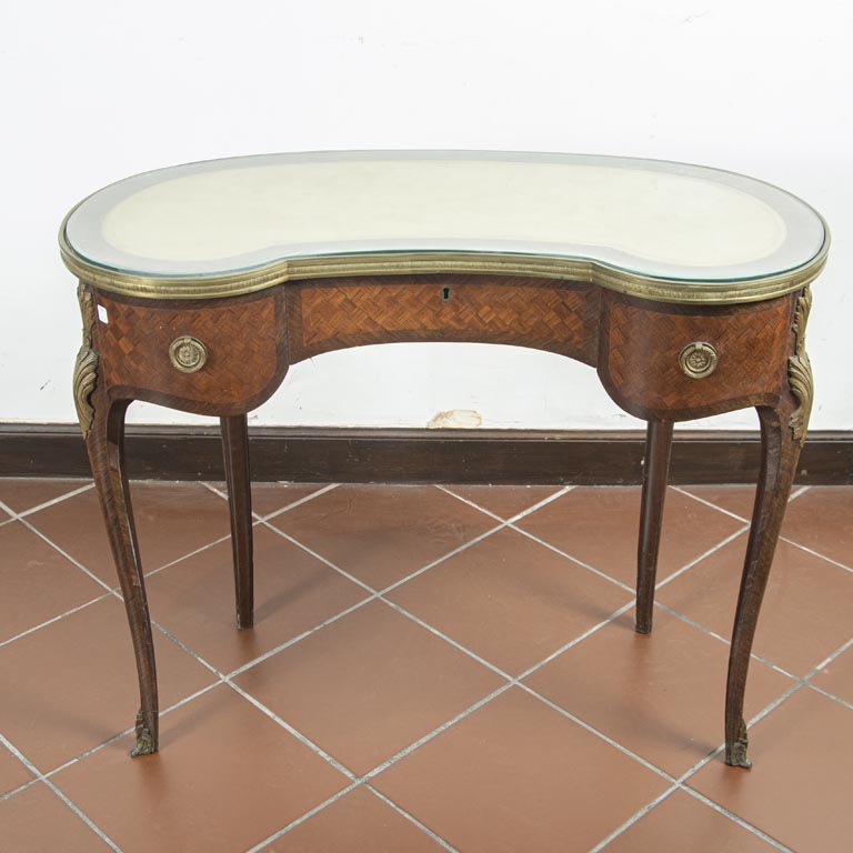 Mesa escritorio Luis XV, riñón, en caoba, aplicaciones de bronce, 2 cajones, tapete de cuero y tapa de vidrio. Detalles en el enchapado - Medidas: 92x39x76cm