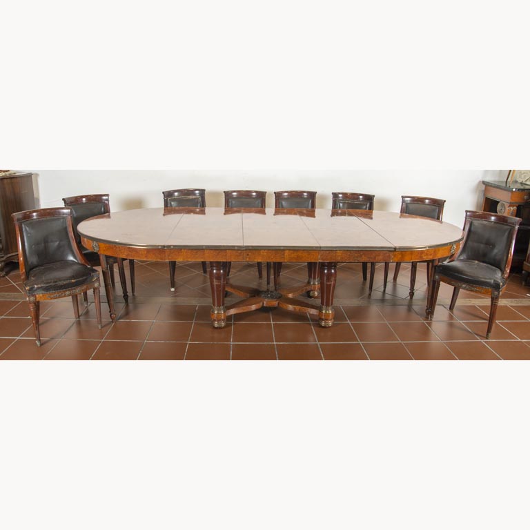 Juego de comedor Imperio en caoba y raíz, aplicaciones de bronce, mesa oval extensible con 3 tablas de alargue y 8 sillas tapizadas en cuero. Las sillas tienen varios detalles en el tapizado - Medidas: Mesa total 300x125x75cm