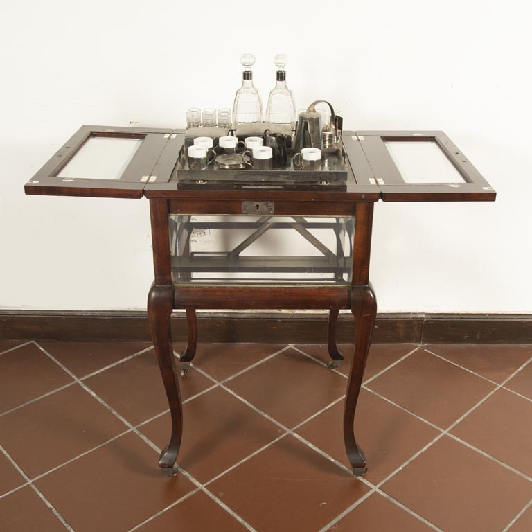 Vitrina inglesa en caoba, vidrios biselados, 2 puertas levadizas, interior con botellones, vasitos, juego de café y juego para fumar - Medidas: 48x48x80cm