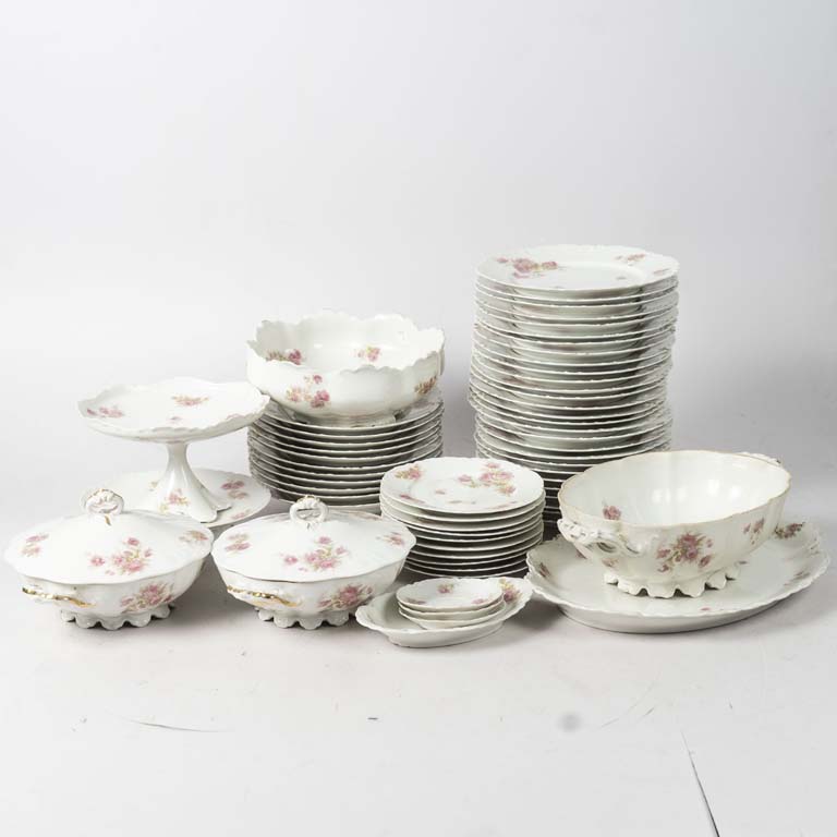 58 Piezas juego de mesa de porcelana Limoge, fondo blanco decorado con flores y borde lobulado. 12 platos llanos con cascadura, 7 platos hondos con cascadura, 3 platos de lunch con cascadura, plato de masas alto con fisura, sopera con fisura y sin tapa, centro con cascadura en la base y fuente con cascadura. - Medidas: Guisera: 28x9cm