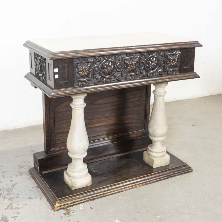Consola de recepción, con doble frente, estilo renacimiento. Tallada, con dos balaustres de mármol, tapa de mármol y dos cajones. Detalles en la madera, avería en el enchapado y detalles en el lustre. Base con enchapado levantado. - Medidas: 100x50x91cm