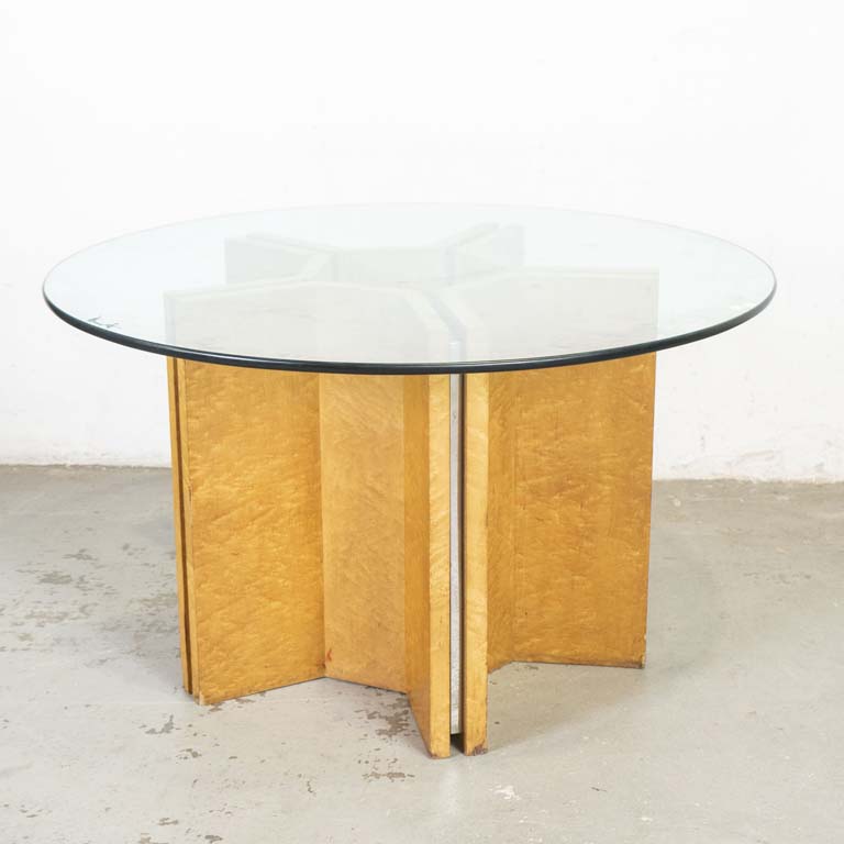 Mesa de comedor circular con: tapa de vidrio y base central. Base (en dos partes) de madera con juntas de metal cromado. Avería en el enchapado a nivel de zócalos. - Medidas: 130 x 75cm