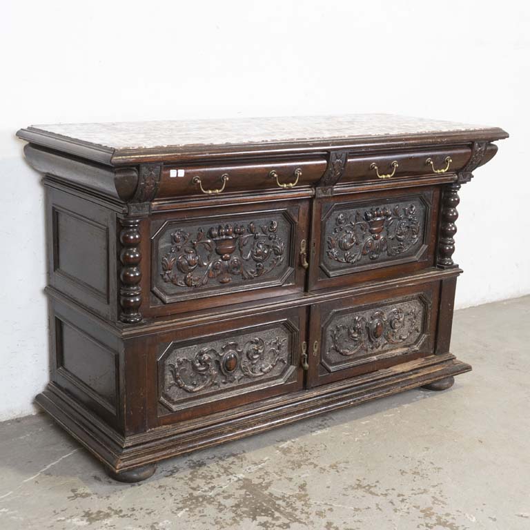 Aparador colonial con frente tallado, con: tapa de mármol, dos cajones y cuatro puertas. Detalles en la madera, cascadura en una esquina y detalles en el mármol. Falta tirador y polillas en la trasera. - Medidas: 156x63x101cm