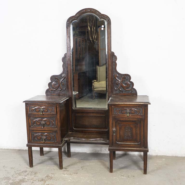 Tocador inglés en roble tallado, con espejo biselado y par de mesitas laterales (una con tres cajones y otra con puerta y cajón). Detalles en el azogue, polillas en la madera y detalles en el lustre. - Medidas: 137x40x180cm