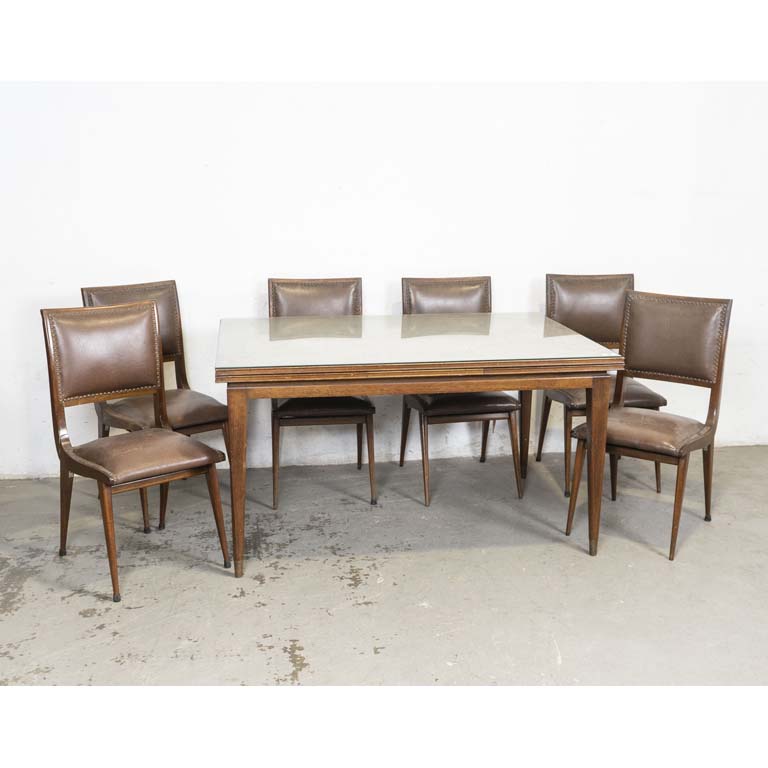 Mesa de comedor americana tiré y seis sillas tapizadas con tachas. Una silla floja, con respaldo quebrado. Detalles en la madera y en el lustre. Tapizados con averías en los bordes. - Medidas: 143 x 41 x 78cm