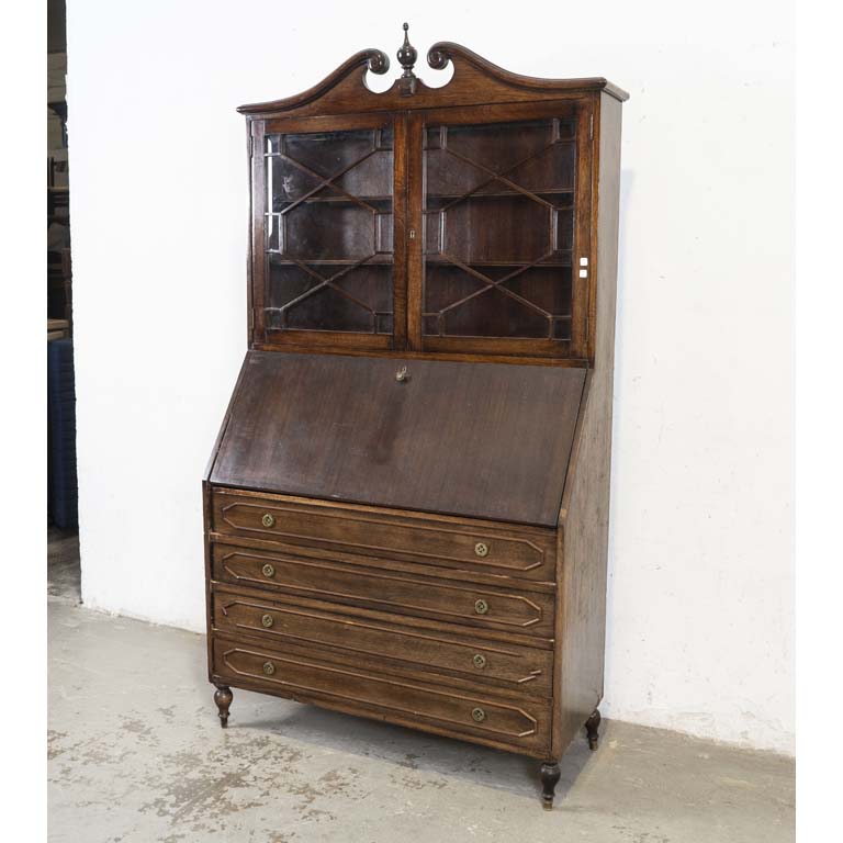 Secretaire inglés, con alzada. Dos puertas de vidrio, puerta abatible horizontal y cuatro cajones. Falta tirador, detalles en el enchapado y en el lustre. Pata suelta. - Medidas: 110 x 43 x 210cm