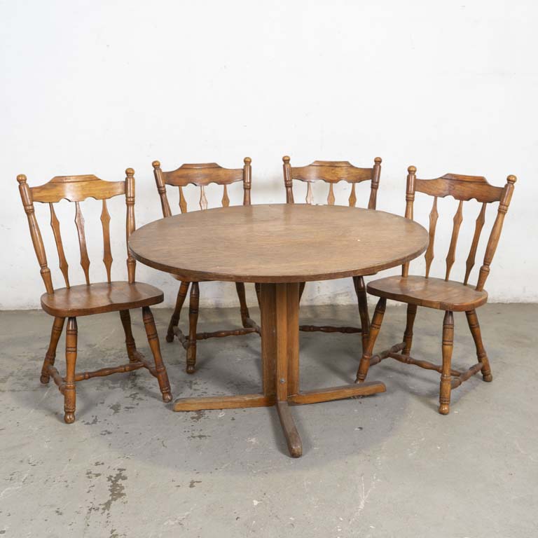 Mesa de comedor circular y cuatro sillas Windsor. Tapa de la mesa con enchapado levantado y pata quebrada. Sillas con asientos reparados en varias partes, con planchuelas metálicas. Detalles en el lustre y en la madera. - Medidas: 110x72cm